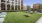 a grassy area with tables and chairs in it and buildings in the background